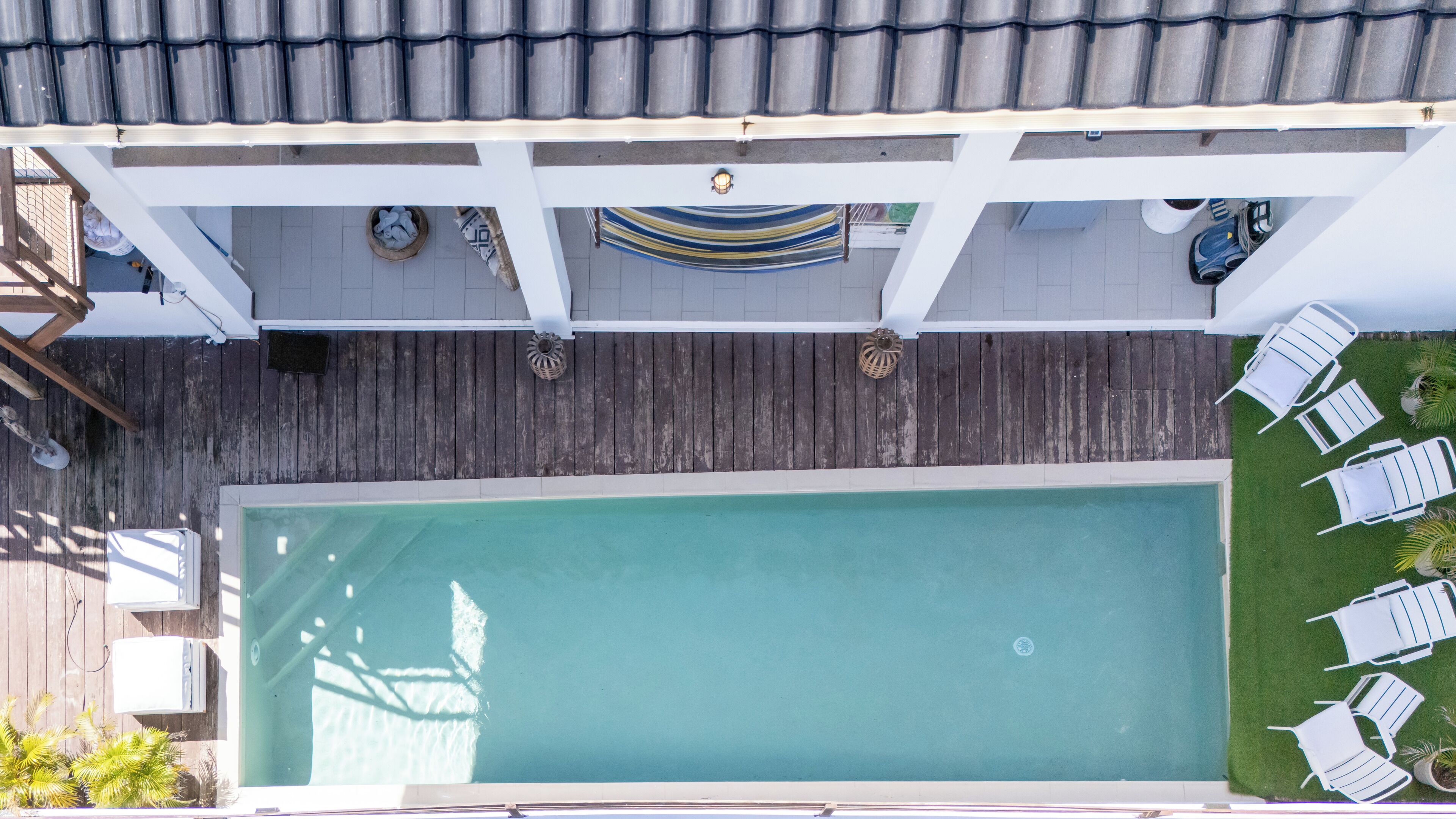 En vy från ovan av en swimmingpool med ett trädäck, omgiven av solstolar och en liten trädgårdsdel.