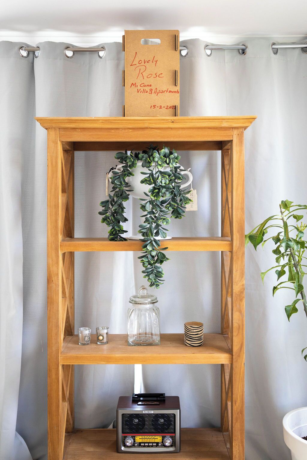 Ein Holzregal mit einem Schild, einer Zierpflanze, einem Glasbehälter und einem Vintage-Radio.