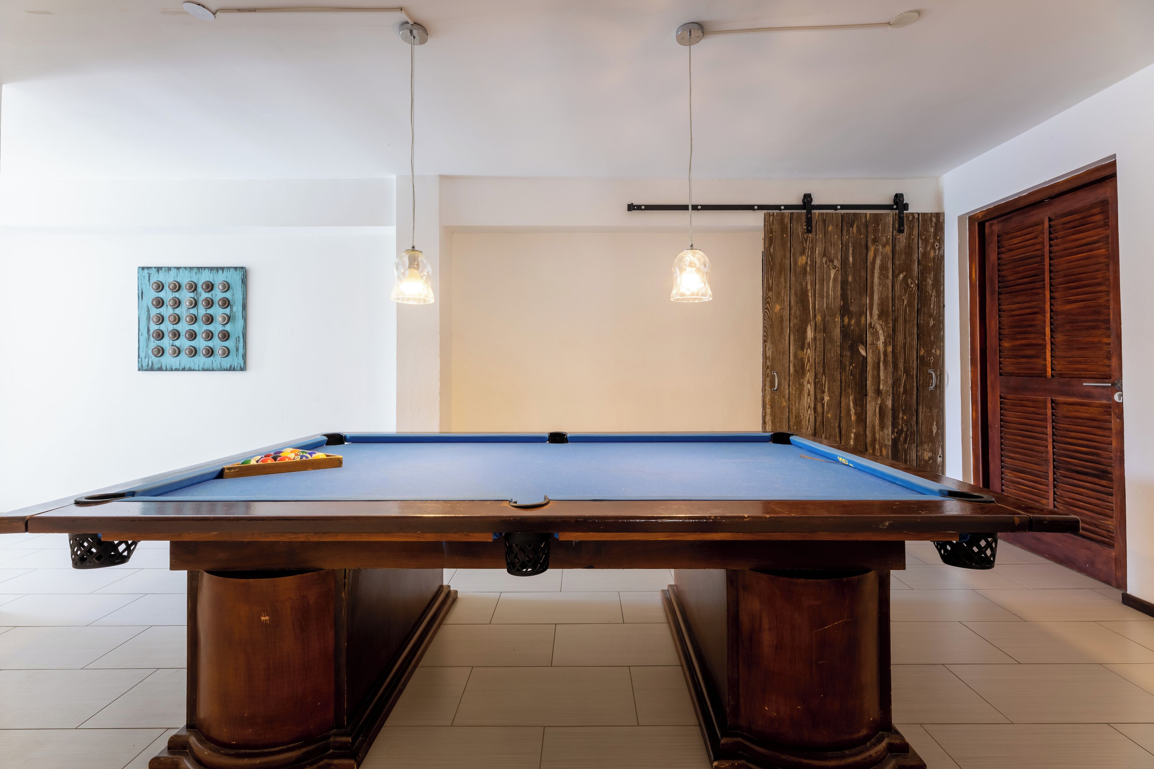 A pool table in a room with white walls, a wooden door, and a blue artwork on the wall.