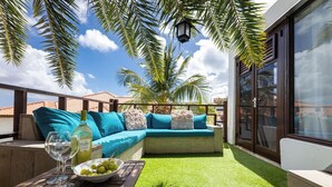 A rooftop terrace with a seating area, a table with a bowl of grapes and a bottle of wine, and a view of palm trees and a clear sky. - Mi Cuna Stays Collection (Jan Thiel)
