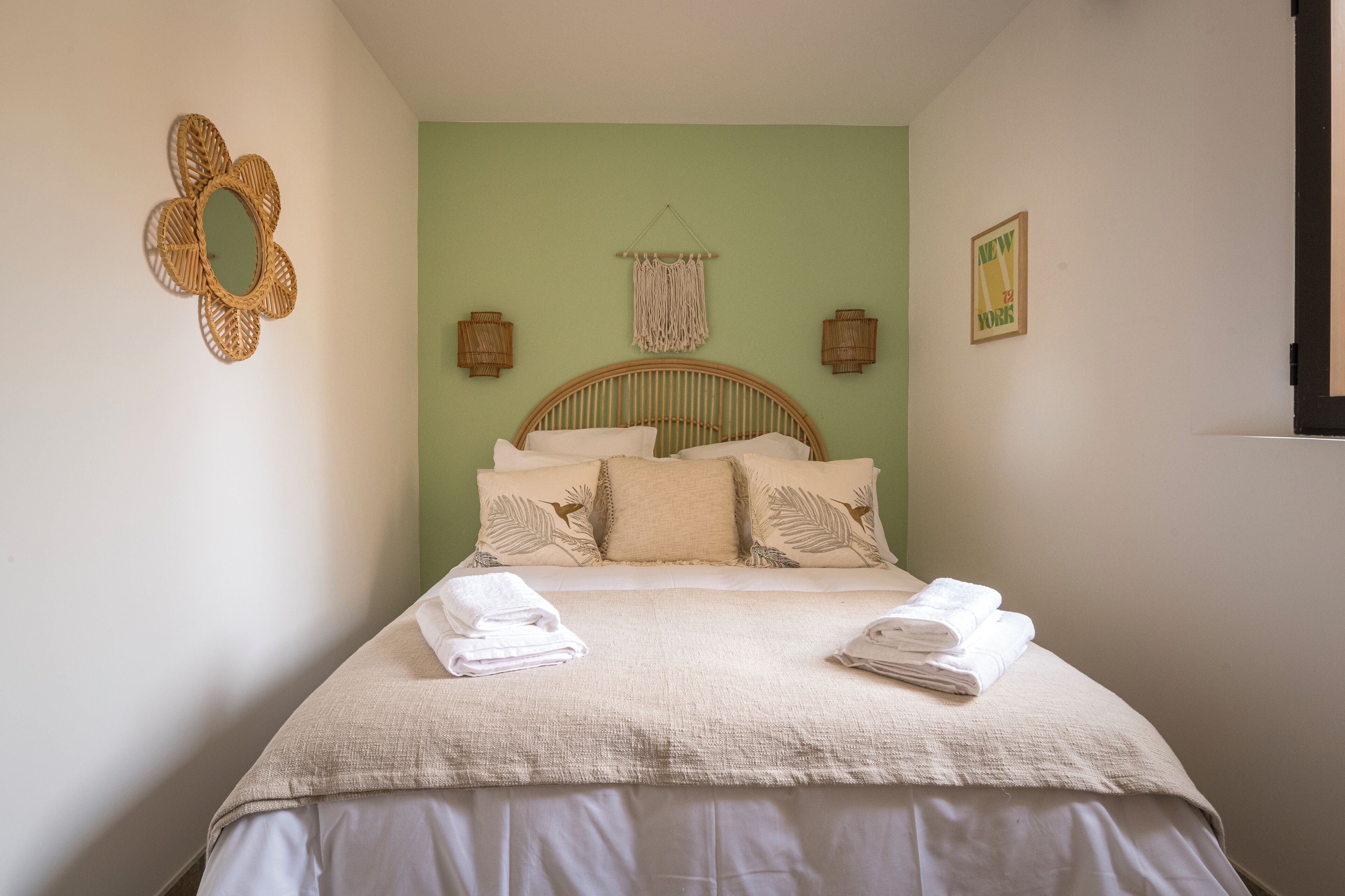 Un lit bien fait, avec une couvre-lit beige et des oreillers, une décoration murale en fibres tressées et un tableau encadré accroché au mur.