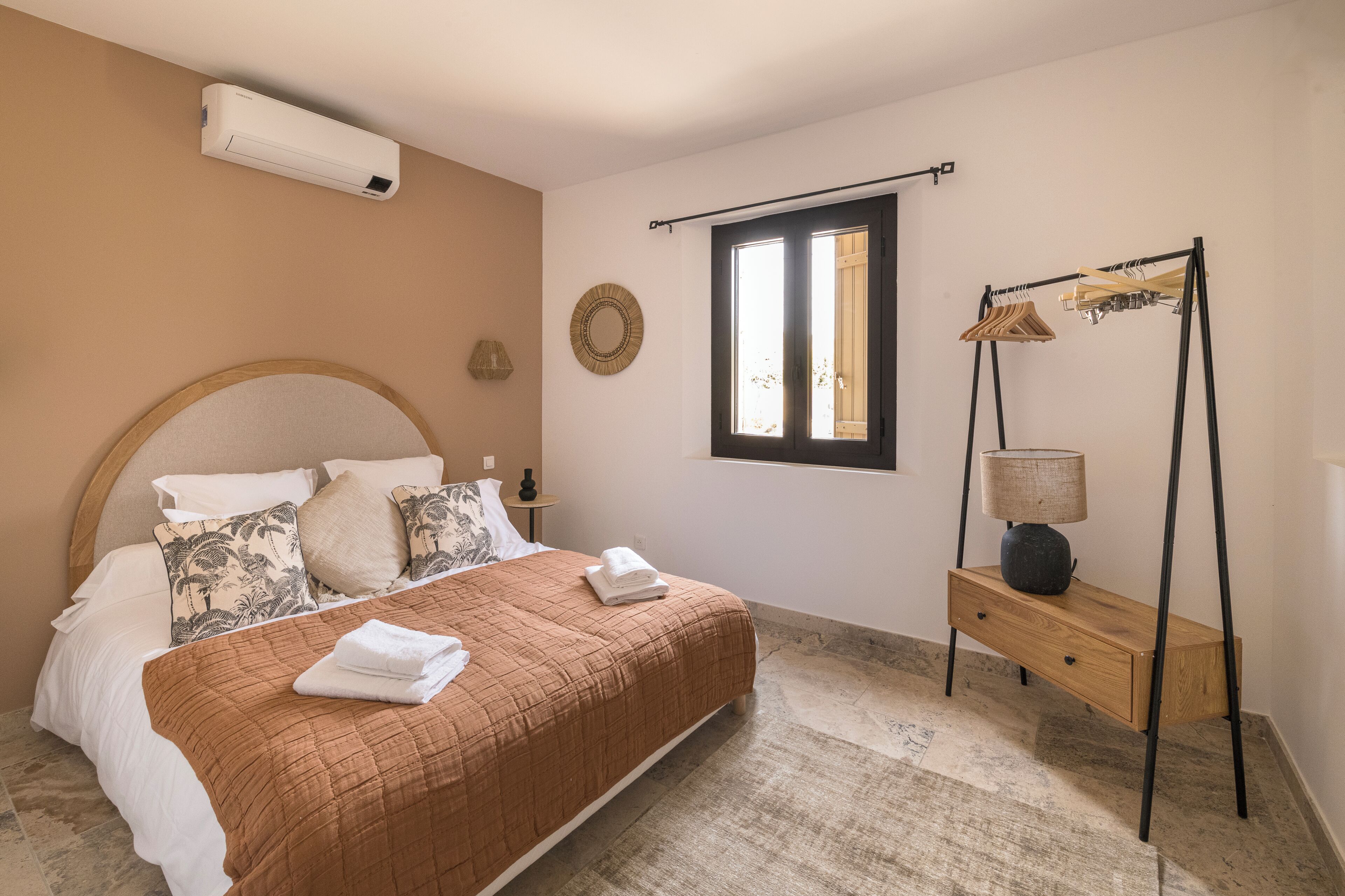 Une chambre à coucher comprenant un lit, une table de chevet, une lampe, une fenêtre et un climatiseur fixé au mur.