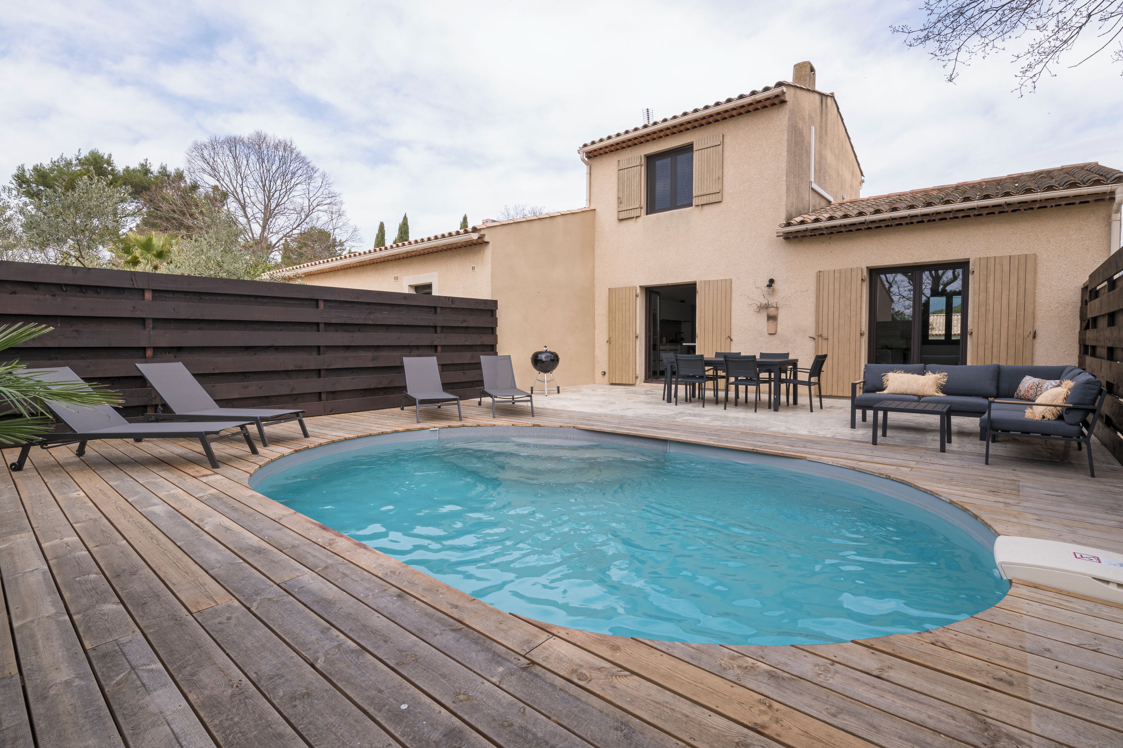 Une terrasse en bois avec une piscine, des chaises longues et du mobilier d’extérieur.