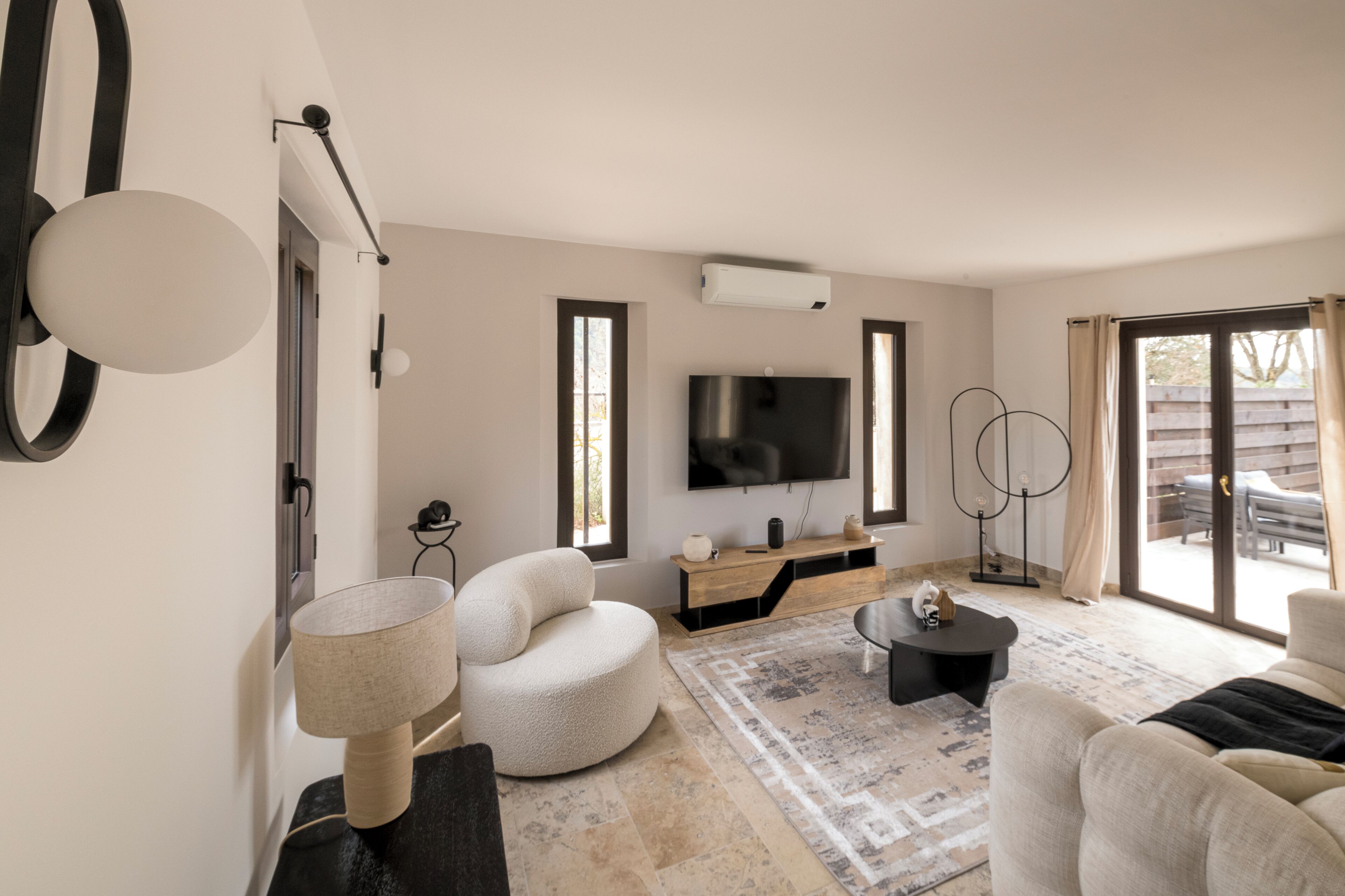A modern living room with a flat-screen TV, a round white chair, a black coffee table, and a patterned rug.