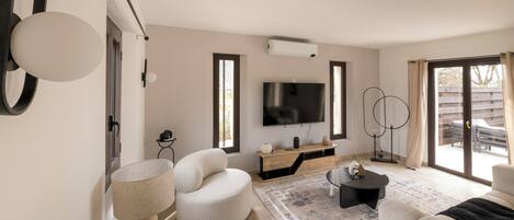 A modern living room with a flat-screen TV, a round white chair, a black coffee table, and a patterned rug.
