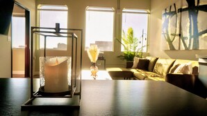 Un soggiorno moderno con un porta candele di vetro su un tavolo di legno, ampie finestre con vista sulla città, un divano e una pianta in vaso.