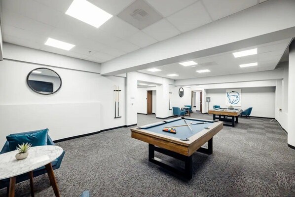 A pool table in a well-lit room with a carpeted floor, a round mirror on the wall, and a door leading to another room. - Chic New York Style 10 Minutes to SNA Disneyland (Santa Ana)