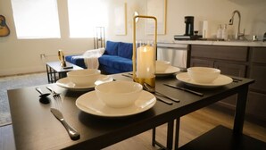 A dining table set with white bowls and plates, a candle, and cutlery in a modern kitchen with a blue sofa and a guitar in the background. - New York Style Home 10 Minutes To SNA Disneyland (Santa Ana)