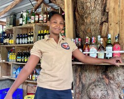A person standing in front of a wooden shelf stocked with various liquor bottles.