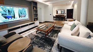 A modern living room with a flat-screen TV, a sofa, a coffee table, and a dining area in the background. - Pradav Apartment (Abuja)