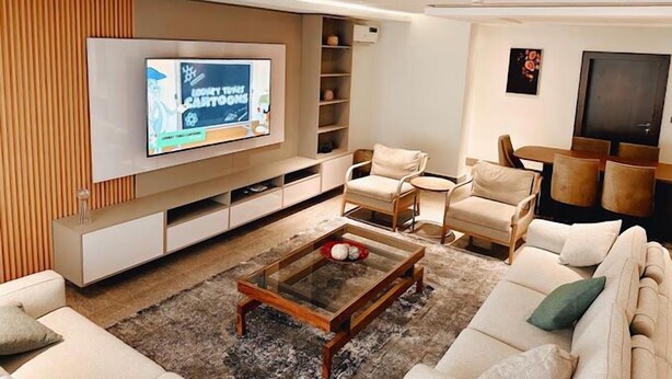 A modern living room with a flat-screen TV, comfortable seating, and built-in shelving. - Pradav Apartment (Abuja)