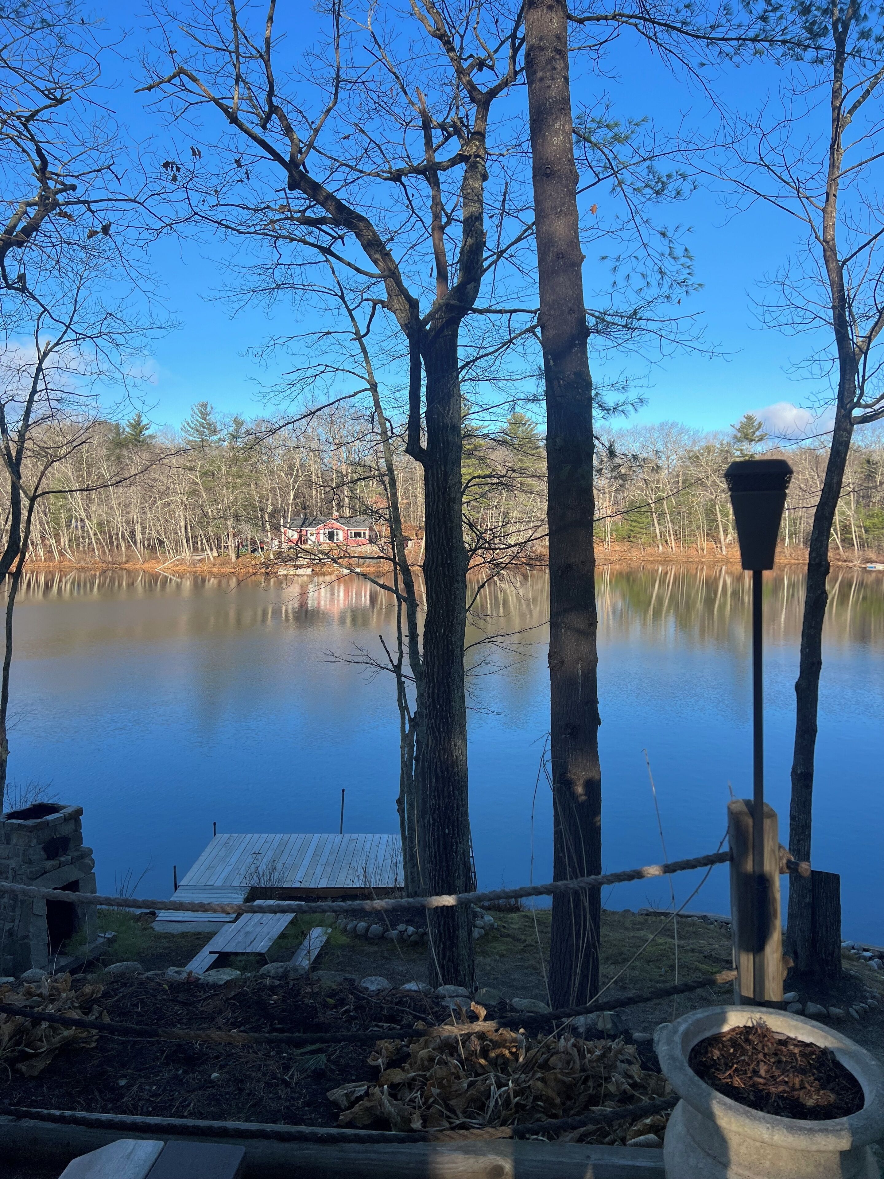 A tranquil lakeside view with a wooden dock, a stone structure, and a lamp post.