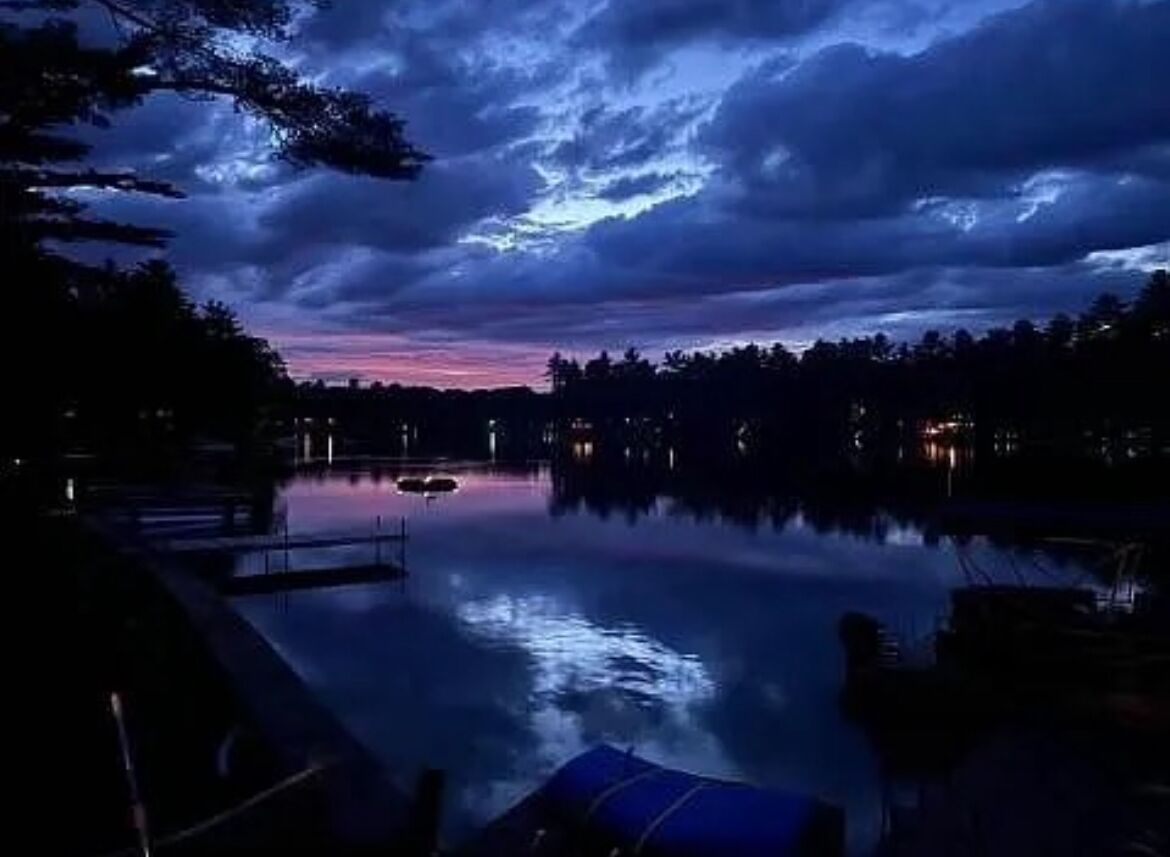 A calm lake at dusk with a dock and trees in the background.