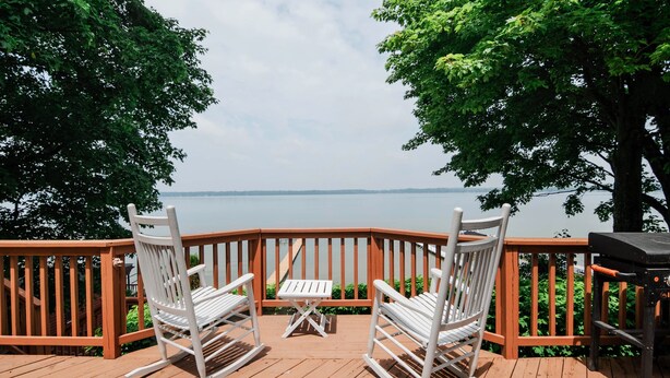 Een houten terras met twee schommelstoelen en een kleine tafel, met uitzicht op een waterpartij.
