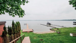 Een gazon met een houten terras dat naar een steiger loopt, uitstrijkend in een rustig meer.