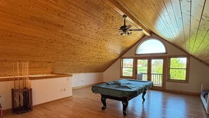 A spacious attic room with wooden floors, a pool table, and a large window. - Beautiful 3 bed, 3.5 bath at Cedar Stone in Eminence MO. Sleeps up to 16 guests. (Eminence)