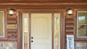 A wooden cabin entrance with a white door, two lanterns, a welcome sign, and a stone wall. - Beautiful 3 bed, 3.5 bath at Cedar Stone in Eminence MO. Sleeps up to 16 guests. (Eminence)