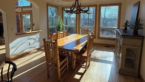 A spacious dining area with a large wooden table and chairs, a chandelier, and large windows offering views of the outdoors. - Beautiful 3 bed, 3.5 bath at Cedar Stone in Eminence MO. Sleeps up to 16 guests. (Eminence)