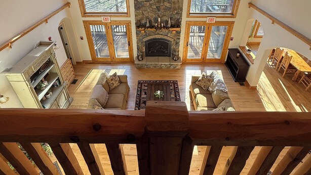 A spacious loft-style room with a stone fireplace, wooden ceiling, and large windows offering a view of the outdoors. - Beautiful 3 bed, 3.5 bath at Cedar Stone in Eminence MO. Sleeps up to 16 guests. (Eminence)