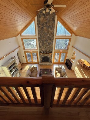 A spacious loft-style room with a stone fireplace, wooden ceiling, and large windows offering a view of the outdoors. - Beautiful 3 bed, 3.5 bath at Cedar Stone in Eminence MO. Sleeps up to 16 guests. (Eminence)