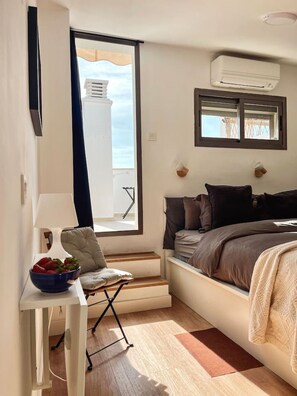 Ein Schlafzimmer mit einem Bett, einem Schreibtisch mit Obstschale, einem Stuhl und einem Fenster mit Blick.