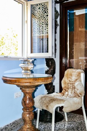 A round wooden table with a glass top, a chair with a fur-like seat, and a window with a decorative screen.