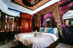 Ein Schlafzimmer mit einem großen Bett, einem verzierten Spiegel und einer Decke mit einem Kronleuchter.