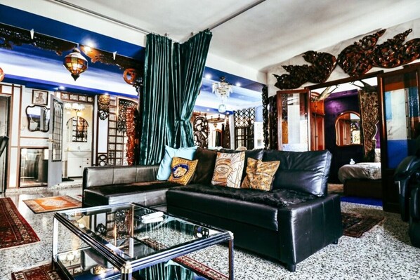 A modern living room with a black leather sofa, a glass coffee table, and a large window with curtains.