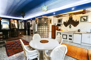 A dining area with a round table and four chairs, a kitchen with white cabinets, and a decorative wall with a guitar and a skull.
