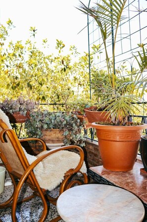 A balcony with potted plants, a wicker chair, and a small table.