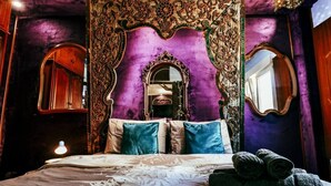 Een slaapkamer met een groot bed, een versierd hoofdeinde en twee spiegels.