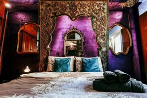 A bedroom with a large bed, ornate headboard, and two mirrors.