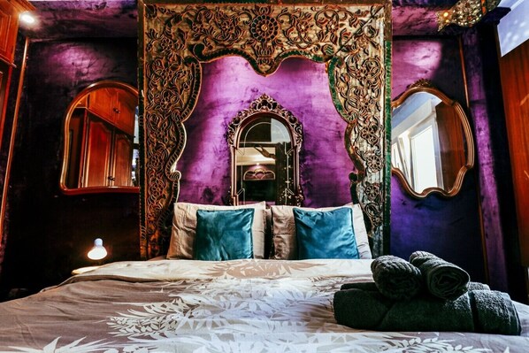 Ein Bett mit Baldachin, ein Spiegel und eine Wand mit floralem Muster.