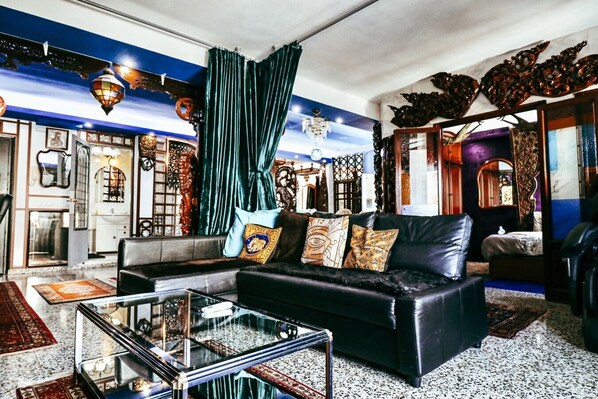 A living room with a black leather sofa, a glass coffee table, and a large window with curtains.