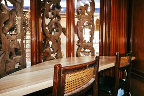 A wooden dining table with chairs, ornate wooden panels, and a view through a window.