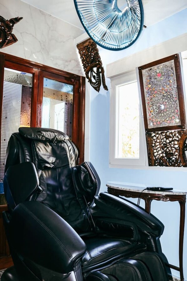 A room with a massage chair, a ceiling fan, a window with a view, and decorative wall art.