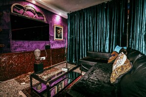 Ein Zimmer mit einem dunkelblauen Samtvorhang, einem schwarzen Ledersofa und einem gerahmten Bild an der Wand.