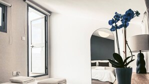 Ein modernes Schlafzimmer mit einem großen Fenster, einem Bett mit weißer Bettwäsche, einem Spiegel, einer Zimmerpflanze und einem Nachttisch mit einer Lampe.