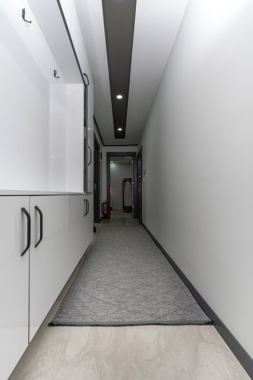 Un pasillo con armarios blancos, alfombra gris e iluminación empotrada en el techo.
