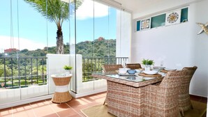 A balcony with wicker furniture, a glass table, and a view of a green landscape. - Mirador Marbella | Pool | Golf | Gym | Sauna (Ojén)