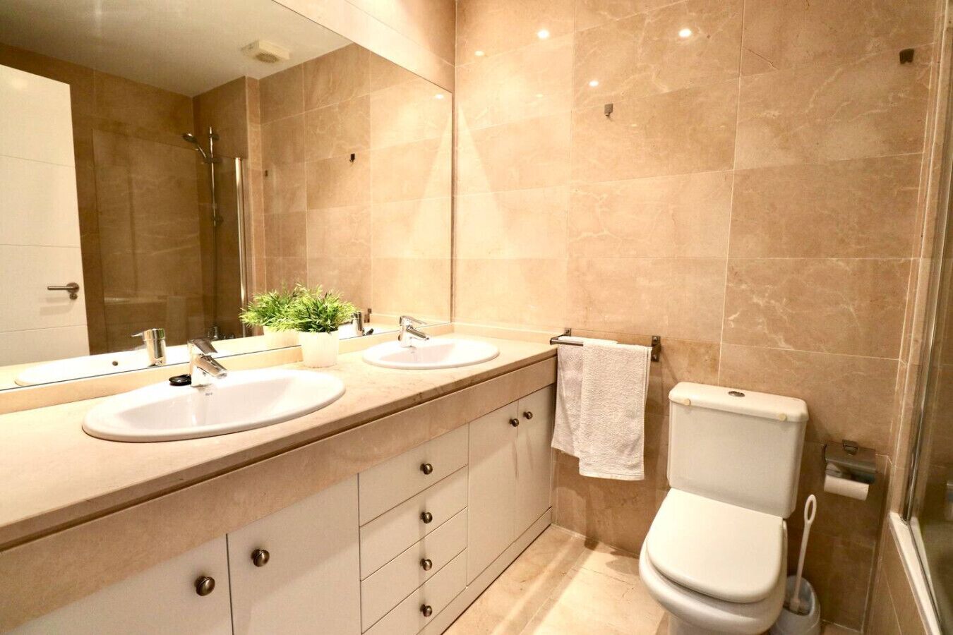 A modern bathroom with two sinks, a toilet, and a shower.