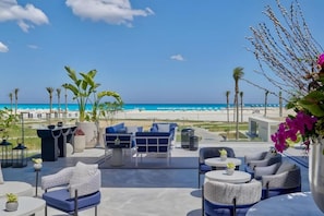 Eine Terrasse mit Sitzgelegenheiten im Freien, Blick auf den Strand und Palmen.