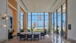 A spacious room with a large window overlooking a beach, a dining area with a table and chairs, and modern pendant lighting. - Magnificent 1-BR Sea view  Address Beach Marassi (El Alamein)