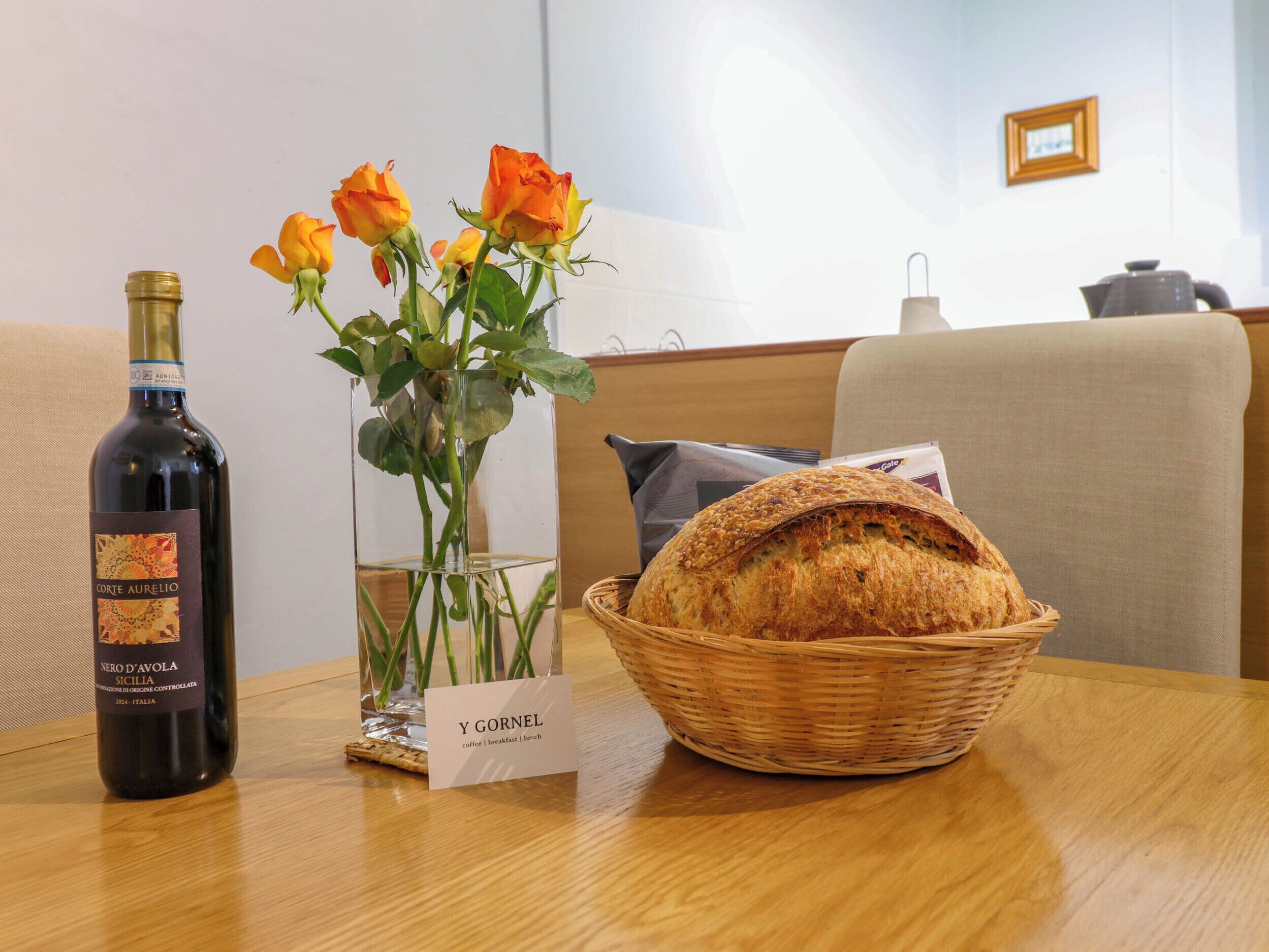 Une table avec une bouteille de vin, un vase de roses, un panier de pain et une pancarte sur laquelle on peut lire « Y GORNEL ».
