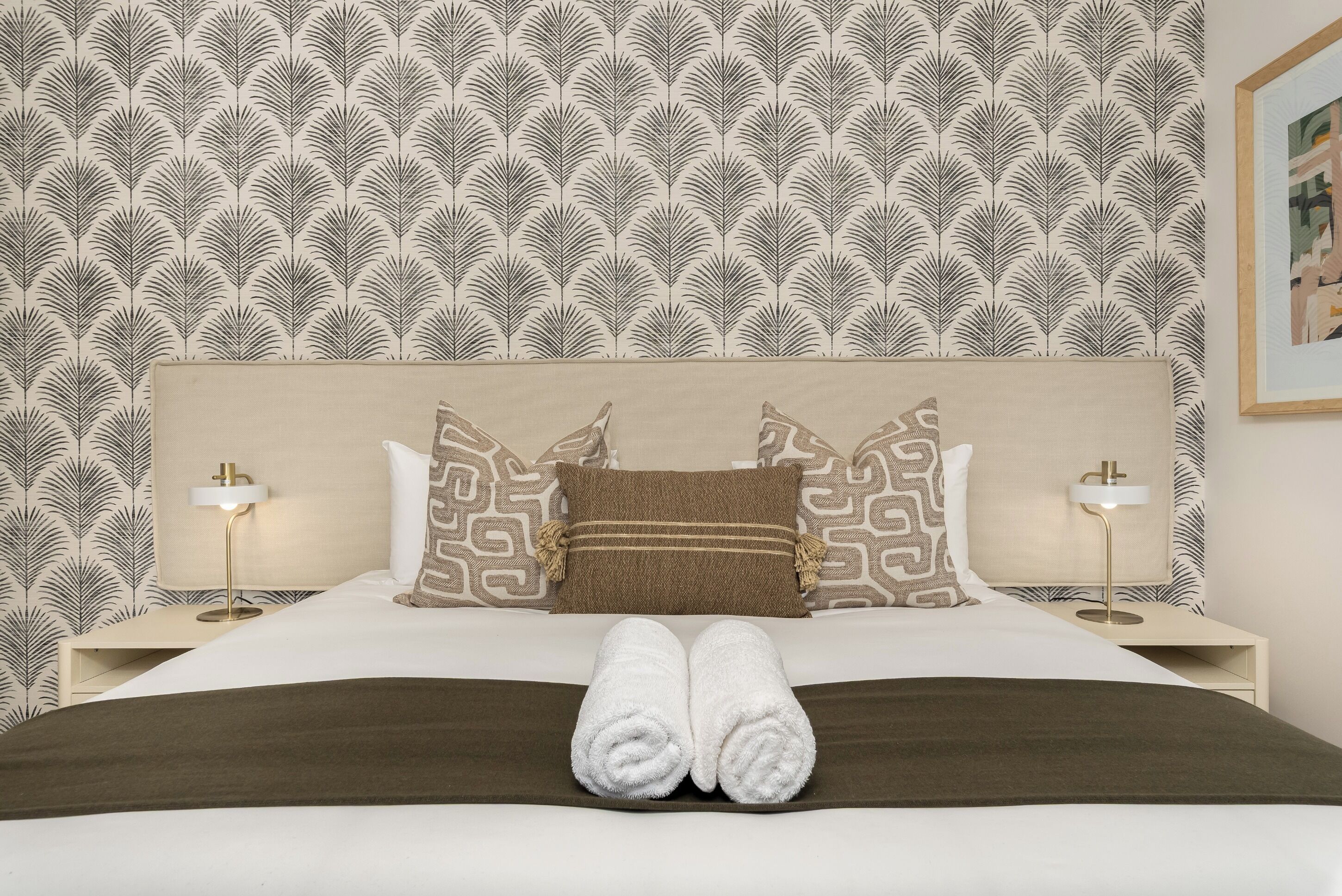 A neatly made bed with a patterned headboard, two bedside lamps, and a brown throw blanket.