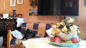 A living room with a sofa, a television, framed artwork on the wall, and a table with a fruit bowl. - PANORAMIC EAGLE - The mountains, 5 minutes from the shops (Montoso)