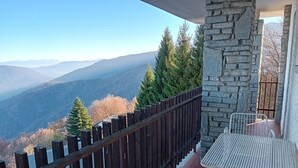 A balcony with a stone wall, a wooden fence, and a metal table and chair. - PANORAMIC EAGLE - The mountains, 5 minutes from the shops (Montoso)