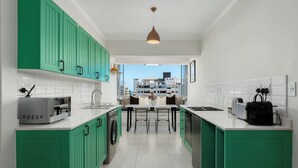A modern kitchen with green cabinets, a central island, and a view of buildings outside. - Heart of Seapoint Hideaway (Cape Town)