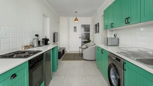 A modern kitchen with green cabinets, a stove, oven, microwave, and dishwasher. There is a small seating area with a table and chairs. - Heart of Seapoint Hideaway (Cape Town)