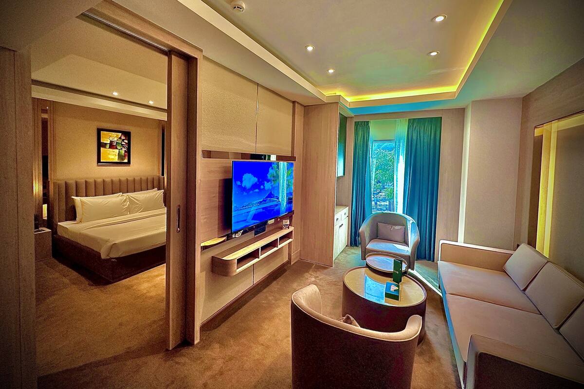 A modern hotel room with a bed, a TV, a sofa, and a coffee table.